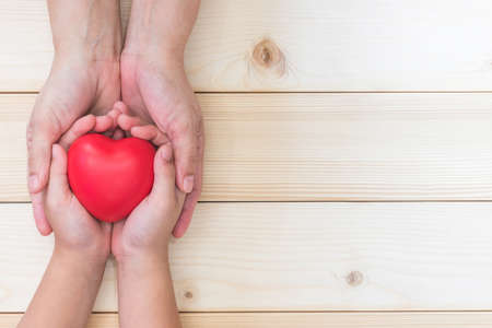 I love you Mom, Mother's Day celebration with woman holds young kid's hands supporting red heart, and charity donation for nursing children conceptの写真素材