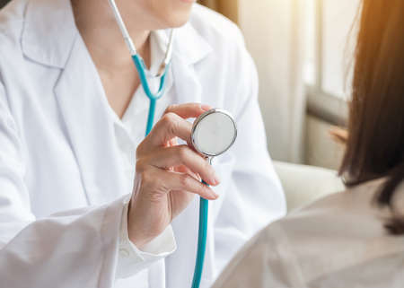 Healthcare concept with cardiologist doctor examining woman patient's heart health diagnosing cardiovascular disease illness symptom using stethoscope in medical clinic or hospital service centerの写真素材