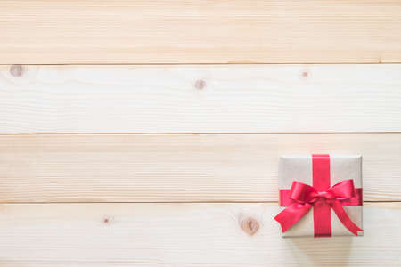 Gift box present with red bow ribbon and brown krafts wrapping paper on white pine wood backdrop for Christmas boxing day, winter xmas holiday seasonal celebration and wedding present backgroundの写真素材
