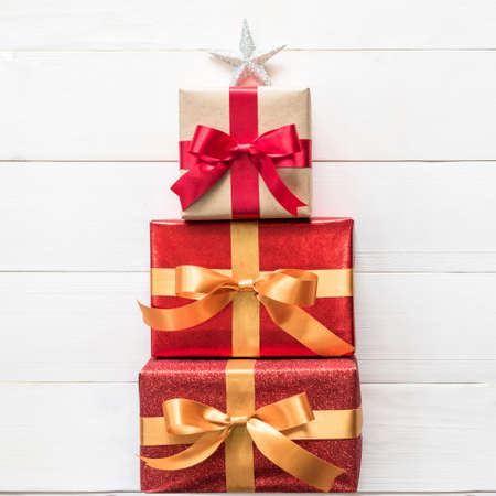 Gift box present stack in Christmas tree shape with red-gold luxury ribbon, star top on white pine wood backdrop for Xmas boxing day and winter holiday seasonal celebration backgroundの写真素材