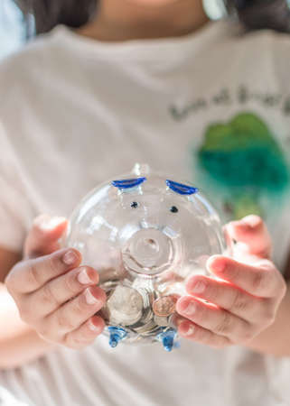 Money saving banking concept with girl kid holding coins in glass piggy bank for educational and family fundの写真素材