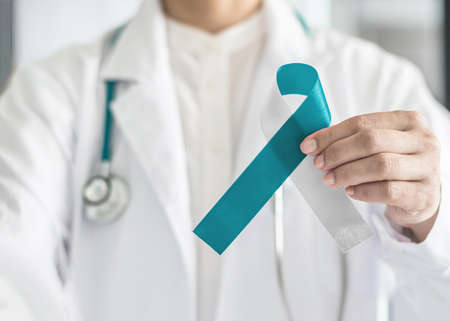 Cervical Cancer awareness with teal and white ribbon symbolic bow color on doctor helping hand support for national cervical cancer awareness month campaign in Januaryの写真素材