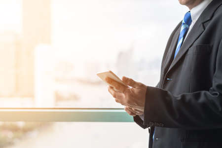 Business man working lifestyle using internet wireless communication via mobile smartphone touch screen and digital online application technology with city office building backgroundの写真素材