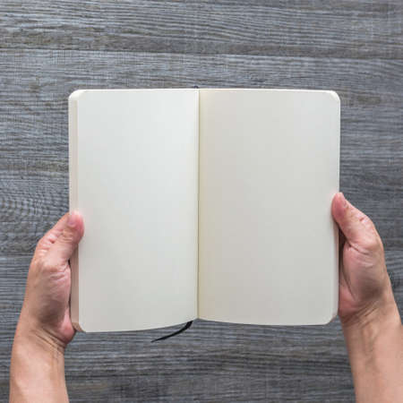 Mockup book, blank open page catalog, magazine, brochure, pocket booklet template paper texture in person's hands on wood tableの写真素材