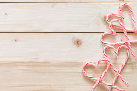 Candy cane in heart love shape on white pine wood knotty table background for Christmas food backdrop, Valentine's day, and sweetest day decoration with copy space flat lay from top viewの写真素材