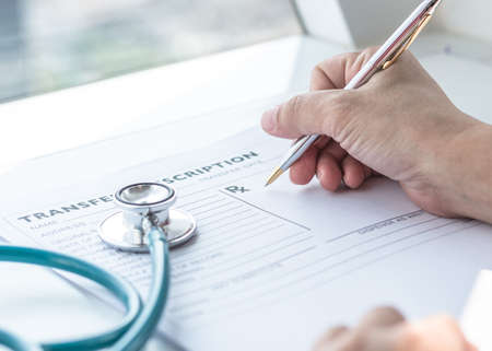 Doctor writing on medical health care record, patients discharge, or prescription form paperwork in hospital clinicの写真素材