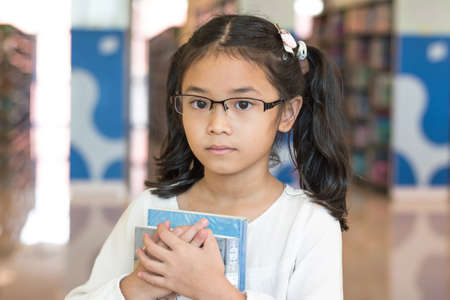 Equal learning opportunity and accessibility in education concept with Asian student kid holding book in libraryの写真素材