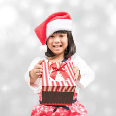 Asian kid with santa claus hat holding gift box giving present on seasonal holidays celebrationの写真素材