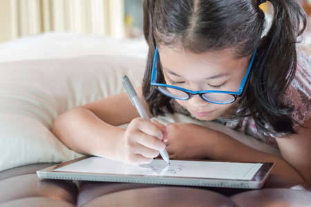 Asian school child girl using smart  tablet device digital technology drawing on innovative...