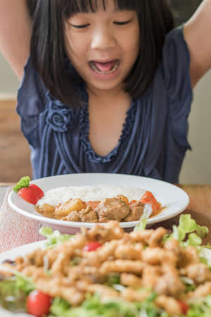 Child appetite concept with happy Asian school girl kid with delicious nutritional meal of food menu for breakfast, lunch, or dinner served with beautiful decoration on kitchen tableの写真素材