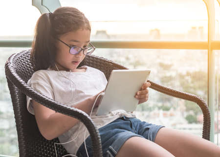Digital technology education concept of school kid lifestyle using internet learning and reading e-book on wireless mobile tablet app for educational studying and playing online game for recreationの写真素材