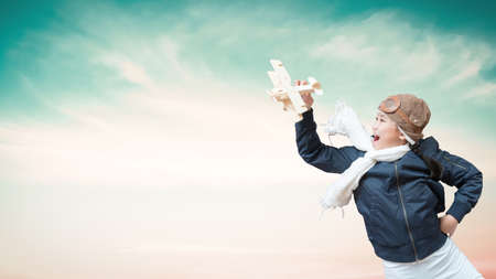 Girl child in pilot costume having fun with creative learning motivation, imagination and inspiration dream high playing flying plane toy over blue sky backgroundの写真素材
