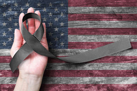 USA United Stated of America 9/11 memorial, Patriot day and National POW/MIA recognition day concept with Black awareness ribbon on people's hand support on American flagの写真素材