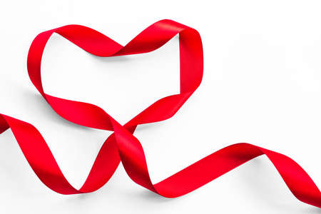 Red satin ribbon bow in heart shape isolated on white background (clipping path), symbolic concept for National heart monthの写真素材