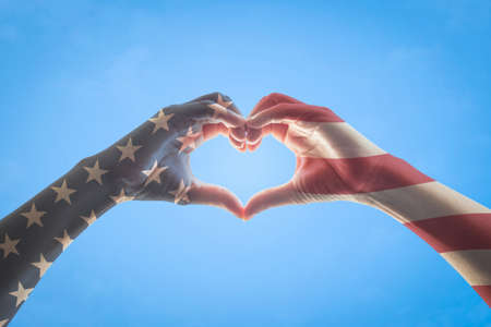 United States of America -USA American flag pattern on people hands in heart love shape isolated on blue sky backgroundの写真素材