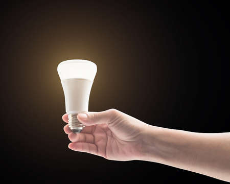Saving energy concept with woman's hand holding LED light emitting diode lightbulb isolated on black background (clipping path)の写真素材