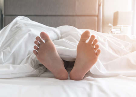 World sleep day, sleeping comfort relaxation and bedtime insomnia concept with young girlâs bare foot laying lazy on bed resting in comfy hotel bedroom on white bed sheetの写真素材