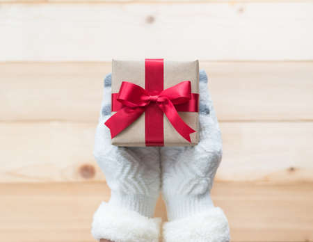 Christmas gift box with red satin ribbon decoration on giver hands giving out on white pine wood table background for boxing day, winter seasonal holiday and new year celebrationの写真素材