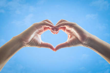 Heart shape woman hands against blue sky backgroundの写真素材