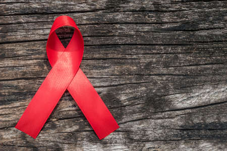 Aids red ribbon for World aids day and national HIV/AIDS and aging awareness month concept. Symbolic satin bow isolated on aged woodの写真素材