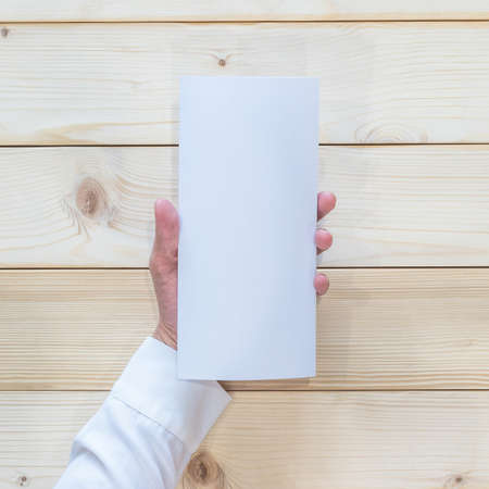 Blank pamphlet mock up cover three-folded flyer A4 paper lay-out template in business person's hand on wood table from top viewの写真素材