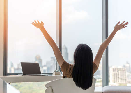 Life balance and summer holiday vacation concept with happy young woman taking a break, celebrating successful work done, casually resting in luxury city hotel workplace with computer laptop on deskの写真素材
