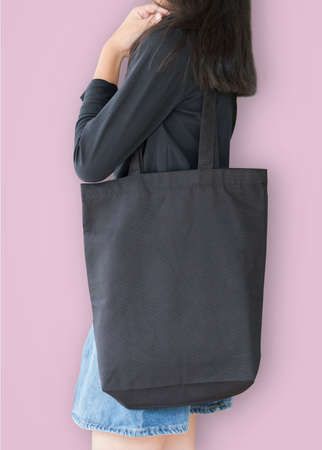 Black tote bag mockup template cotton canvas fabric texture on girl shoulder (isolated with clipping path) on pastel pink backgroundの写真素材