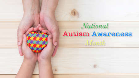 National Autism Awareness month concept with puzzle or jigsaw pattern on heart with autistic child's hands supported by nursing family caregiverの写真素材