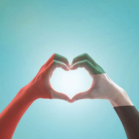 UAE, United Arab Emirate national flag pattern on people's hands in heart shape on blue mint sky backgroundの写真素材