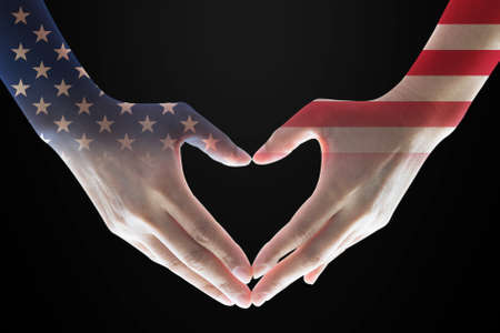 United States of America flag pattern on woman's hands in heart shape on black backgroundの写真素材