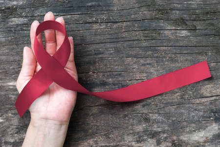 Burgundy ribbon awareness for multiple myeloma cancer awareness and Sickle-Cell Anemia on person's hand support old aged woodの写真素材