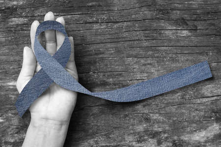 Blue jeans denim ribbon (isolated with clipping path) on helping hand support and aged wood for genetic disorder awareness and children's rare disease illnessの写真素材