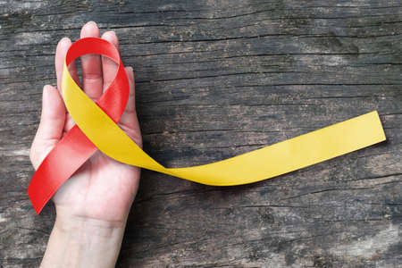 World hepatitis day and HIV/ HCV co-infection awareness with red yellow ribbon    on person's hand support and old aged woodの写真素材