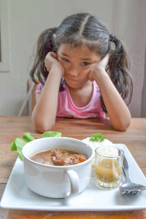 Asian kid getting bored of food refusing meal with appetite loss, no hungry eating habit (focus on food in dish)の写真素材