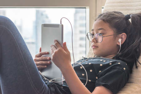 Digital technology lifestyle of school girl child or student using wireless internet for distance learning application and reading e-book app on mobile ipad smart device multimedia computer tabletの写真素材