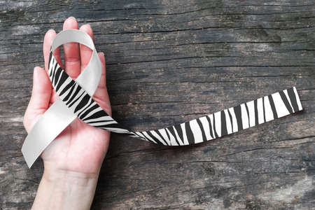 Carcinoid Cancer Awareness ribbon zebra stripe pattern on helping hand support and old aged woodの写真素材