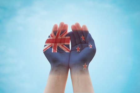 New Zealand flag pattern on people hands in prayer, blue cloud sky backgroundの写真素材