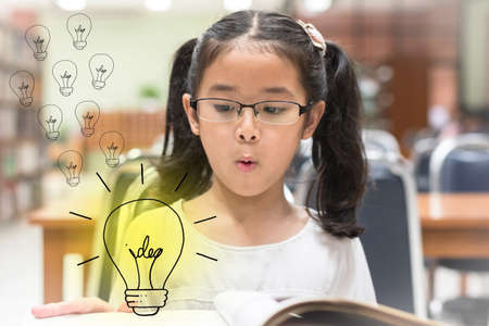 Innovative creative idea for copyrights law concept with kid surprised reading book with lightbulb in libraryの写真素材