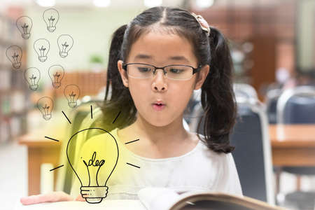 Innovative creative idea for copyrights law concept with kid surprised reading book with lightbulb in library