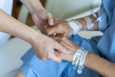Elderly senior aged patient on bed with geriatric doctor holding hands for trust and nursing health care, medical treatment, caregiver and in-patient ward healthcare in hospitalの写真素材