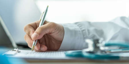 Medical doctor writing on patient personal health care record discharge form, or prescription paperwork in hospital office, clinic center for healthcare and life insurance conceptの写真素材
