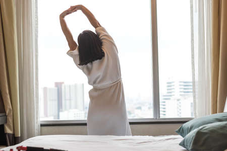 Easy lifestyle Asian woman waking up in weekend morning taking some rest relaxing in comfort city hotel room enjoying world lazy day, having happy life quality balance conceptの写真素材