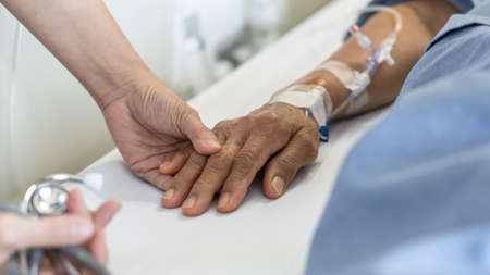 Elderly senior aged patient on bed with geriatric doctor holding hands for trust and nursing health care, medical treatment, caregiver and in-patient ward healthcare in hospital の写真素材
