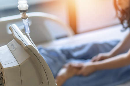Saline intravenous (IV) drip for medical treatment and nursing patient in hospital with blurred family caregiver or nurse caregiving ill patient on bed in wardの写真素材
