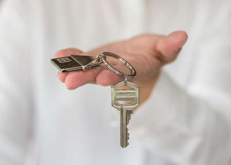 House key in real estate sale person, landlord or home Insurance broker agent's hand giving to buyer customer for new family owner, property assurance conceptの写真素材