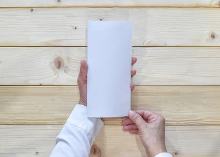 Trifold pamphelt mock up flyer brochure design A4 size paper in business man's hand for template illustration mockup, flat lay on wood table from top viewの写真素材