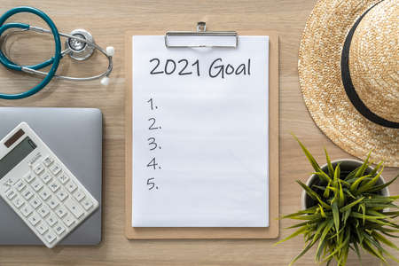 2021 goals on clipboard medical note pad for new year reminder list of yearly planner, health plan for work-life balance on desk background with computer, calculator, travel hatの写真素材