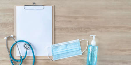 Medical notepad clipboard background with blank note pad paper for patient health exam in new normal lifestlye with hand sanitizer and face mask on doctor work desk for hygiene and covid-19 preventionの写真素材