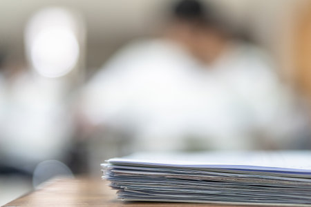 Exam answer sheet pile, blurry application document paperwork stack on office work table in examination room or classroom with blur education background school class university students taking testの写真素材