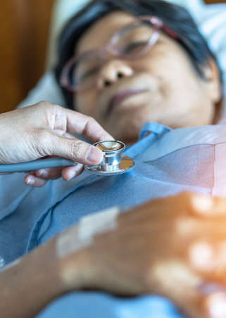Hospitalized elderly patient, senior old aging woman laying on bed with cardiologist doctor or...